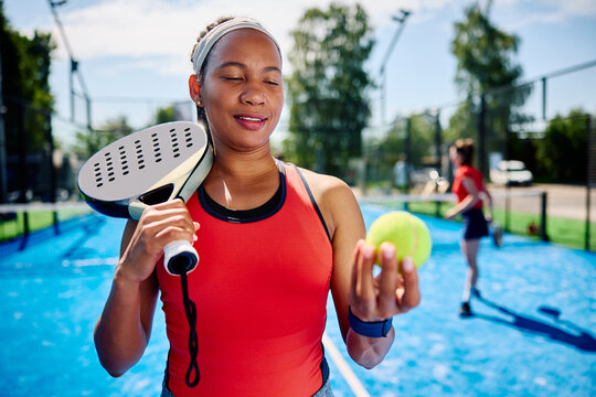 Black athletic woman preparing to serve during doubles match on outdoor court.
