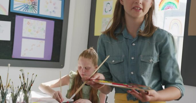 Video of concentrating caucasian schoolgirl standing at easel painting in art class, copy space