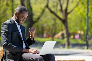 African american businessman working on laptop in the park and looking contented