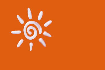 Sunscreen cream in a sun shape on orange background. Creative idea of suntan lotion cream. Sun ultraviolet protection concept.