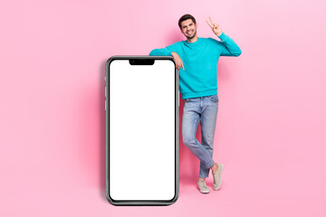 Full size photo of handsome young guy beaming smile show v-sign vertical banner wear trendy blue clothes isolated on pink color background