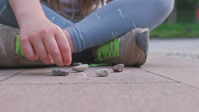 Caucasian Girl Mastering Dexterity Game of Jackstones Scatter Jacks Knucklebones using Small Rocks