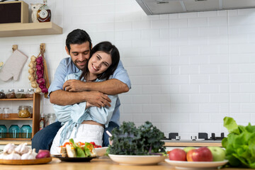 Attractive young couple embracing and cooking together in the kitchen - 621813400