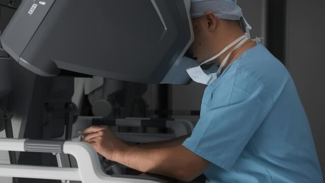 Doctor uses innovative robotic equipment to perform surgery remotely. Process of using stereoscopic monitor to watch and control surgical manipulators in operating room of modern clinic