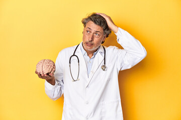 Doctor holding a brain model, yellow studio backdrop being shocked, she has remembered important...