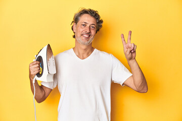 Man with iron in hand on a yellow background showing number two with fingers.