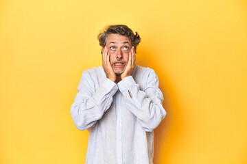 Middle-aged man posing on a yellow backdrop whining and crying disconsolately.