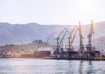 Seascape with loading cranes and a ship against the background of mountains in the rays of the morning sun