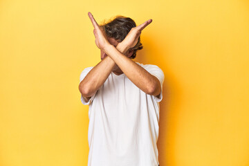 Middle-aged man posing on a yellow backdrop keeping two arms crossed, denial concept.