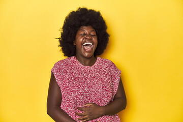 African-American woman with afro, studio yellow background laughs out loudly keeping hand on chest.