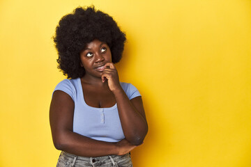 Fototapeta na wymiar African-American woman with afro, studio yellow background relaxed thinking about something looking at a copy space.