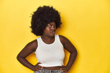 African-American woman with afro, studio yellow background confused, feels doubtful and unsure.