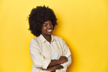 Fototapeta na wymiar African-American woman with afro, studio yellow background suspicious, uncertain, examining you.