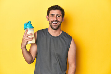 Fit man with protein shake, yellow studio background happy, smiling and cheerful.