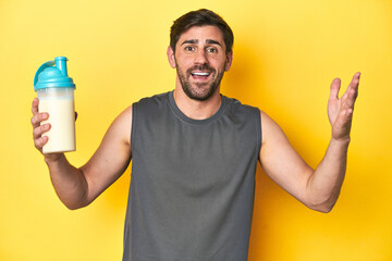Fit man with protein shake, yellow studio background receiving a pleasant surprise, excited and...