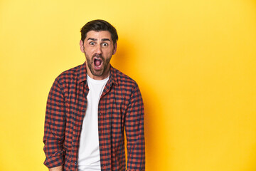 Caucasian man in red checkered shirt, yellow backdrop shouting very angry, rage concept, frustrated.