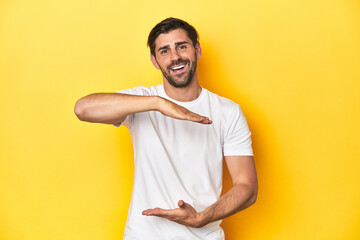Caucasian man in white t-shirt on yellow studio background holding something with both hands,...