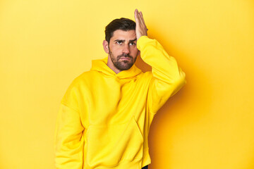 Fototapeta premium Man in yellow hoodie, monochrome studio backdrop forgetting something, slapping forehead with palm and closing eyes.