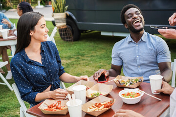 Multiracial couple having fun eating at food truck restaurant outdoor - Focus on african man hand holding phone