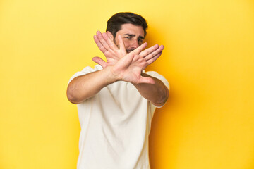 Caucasian man in white t-shirt on yellow studio background doing a denial gesture