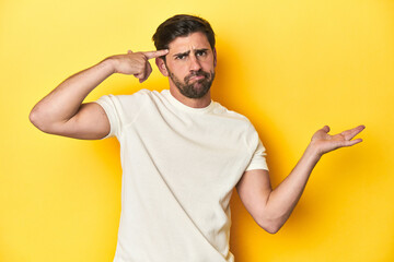 Fototapeta premium Caucasian man in white t-shirt on yellow studio background holding and showing a product on hand.