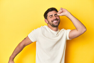 Fototapeta na wymiar Caucasian man in white t-shirt on yellow studio background celebrating a special day, jumps and raise arms with energy.