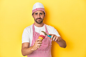 Ice-cream man preparing a delicious treat on yellow studio background.