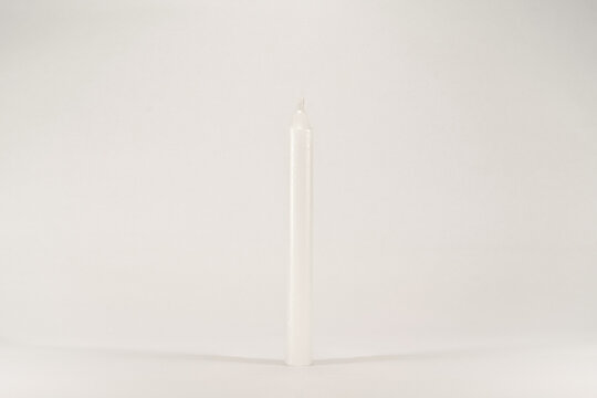 A white wax unlit candle without fire isolated on white background with low light shadow