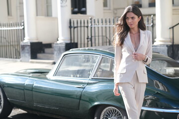 Gorgeous lady in elegant suit with classic sport car in background.