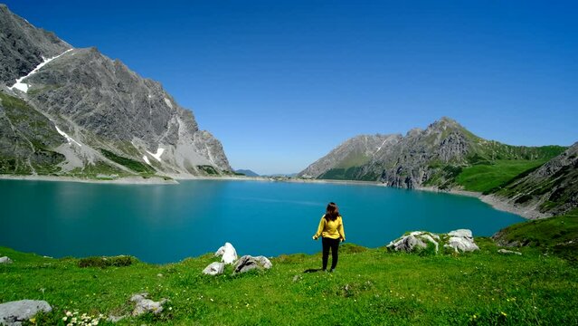 A woman is watching the beautiful blue lake surrounded by a mountain.