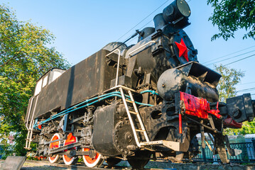 An old steam locomotive on a pedestal. History of railway locomotives. The locomotive is black with a red star on the front.