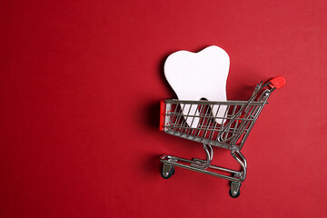 Tooth model with shopping trolley on a red background.