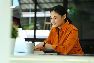 Pretty young businesswoman in smart casual wears using laptop at modern office