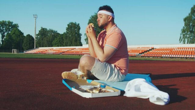 overweight caucasian man in the stadium enjoying a burger after workout. healthy eating and fitness
