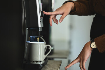Side view of woman preparing fresh aromatic coffee, using a coffee machine maker in cozy office...