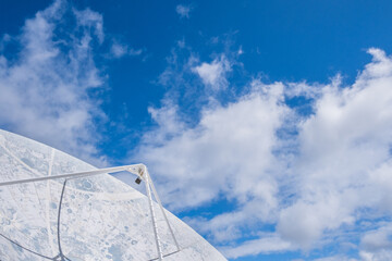 View of a large satellite dish to observe the cosmos, decorated with the lunar topography, with large white clouds in the background.