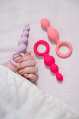 A woman chooses anal beads from a set while lying in bed. 