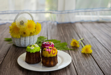 Three cupcakes with floral early-color decor on a white plate and yellow flowers on a wooden background.