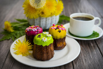 Three cupcakes with floral early-color decor on a white plate and yellow flowers on a wooden background.
