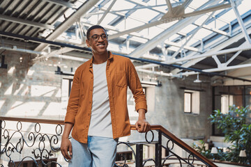 Young smiling freelancer standing on coworking background and looking at camera