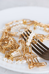 Jewelry bijouterie gold chain and pearl necklace with fork instead of food in a plate. Shopaholism, waste of money, luxury concept.