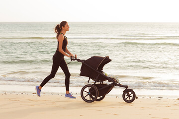 Sporty mom with a stroller is running on the beach.