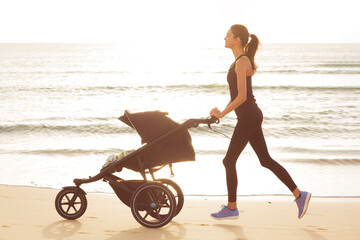 Sporty mom with a stroller is running on the beach.