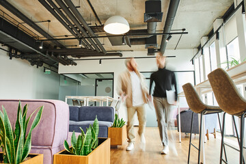 motion blur of entrepreneur with laptop walking next to business partner and discussing startup in office lounge with high tech interior, modern furniture, natural plants, dynamic business concept