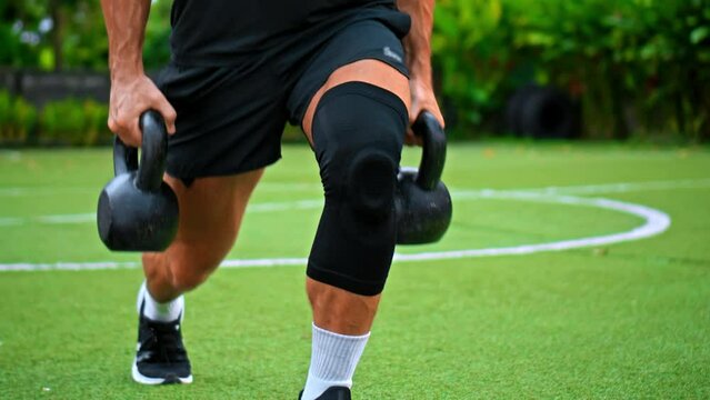 European athlete lifting weights on green grass, with the support of a knee brace for hand. Focuses on fitness, training, strength, and muscle development.