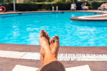 Fototapeta na wymiar Men's legs lying on a deck chair overlooking the water, sunbathing by the pool of the hotel resort