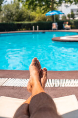 The legs of a man relaxing on a deck chair overlooking the water, sunbathing by the pool