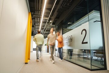 motion blur of energetic and ambitious businessmen walking in corridor of modern coworking...
