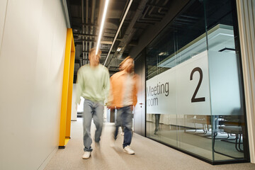 long exposure of two successful business partners walking along meeting room in corridor of contemporary office with coworking environment and high tech interior, dynamic business concept