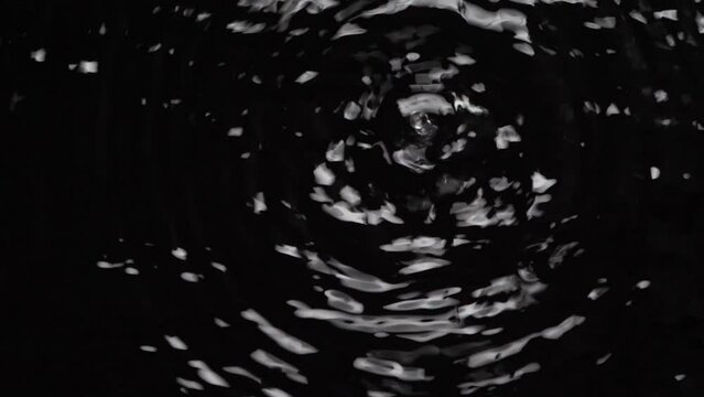 Top view slow motion speed scene of chaotic wave pattern when droplets dropping on surface of water isolated on black background, raindrop falling down to the ground in the night